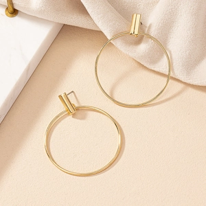 Close-up of golden geometric hoop earrings with rectangle studs on beige textured fabric