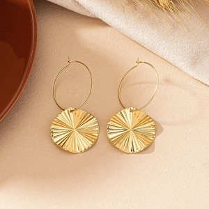 Detailed view of gold earrings with sunburst texture disks in a warm lifestyle setting