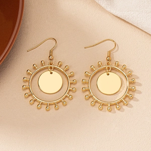Détail de boucles d'oreilles créoles dorées au design radial sur fond texturé élégant