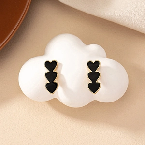 Macro view of triple black heart earrings with gold trim on cloud decor