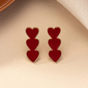 Elegant triple red heart earrings with golden metal edges on a textured beige background