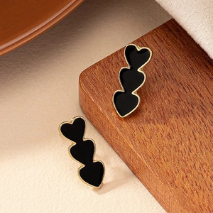 Three-tier black heart stud earrings with gold trim on a minimalist wooden display