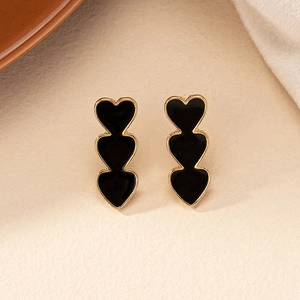 Close-up of triple black heart stud earrings with golden metal frame on beige surface