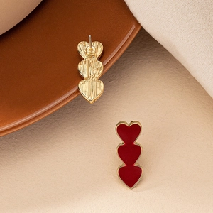 Macro shot showing front and back details of red triple heart earrings on beige fabric