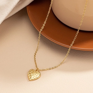 Detail shot of a golden heart pendant with a textured plaid pattern on a ceramic plate
