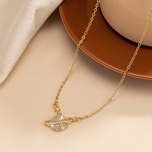 Élégant collier pendentif planète Saturne en or avec cristaux sur fond chaleureux