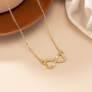 Détail du collier cœur infini doré serti de diamants sur une surface texturée beige