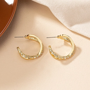 Detail of twisted gold C-hoop earrings with sparkling pavé zircons on a beige texture