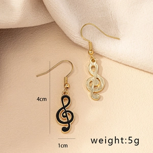 Asymmetric gold and black G-clef music note earrings on textured beige background