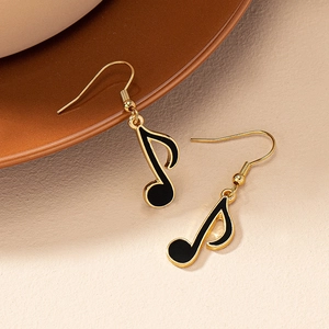 Close-up of golden music note earrings with black enamel inlay on a ceramic plate