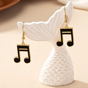 Detail of golden musical note earrings with black enamel on a ceramic holder