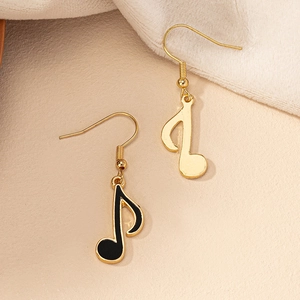 Detail view of gold music note earrings with black enamel on a soft beige background