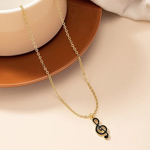 Collier en chaîne dorée avec pendentif note de musique en émail noir sur un plateau élégant