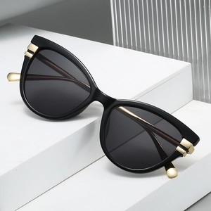 Classic black cat-eye sunglasses with gold metal accents on white geometric podium