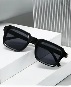 Detail of square black sunglasses with gold metal hinges on a geometric white display
