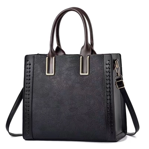 Close-up of floral embossed texture and golden metal hardware on black leather tote