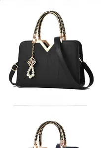 Detail of black textured handbag featuring gold V-hardware and pearl pendant charm