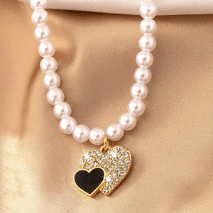 Vue macro d'un collier de perles avec des pendentifs cœurs superposés en or, noir et diamant