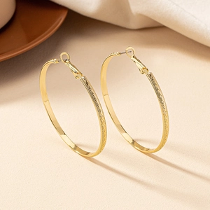 Elegant gold-tone hoop earrings with continuous wave texture on a soft beige background
