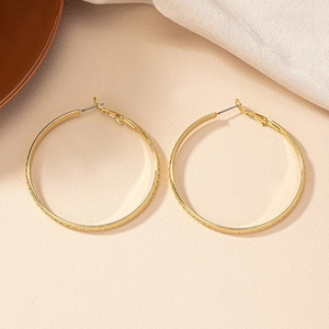 Detail of large gold hoop earrings with textured finish on warm sand background