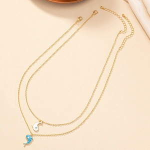 Collier double rang doré avec pendentifs dauphin bleu et blanc sur fond texturé beige