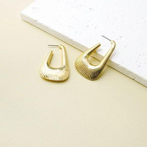 Retro golden geometric earrings with textured radial lines on a minimalist stone display