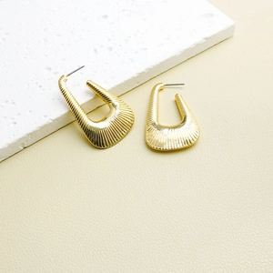 Golden irregular geometric hoop earrings with textured radial patterns on stone background