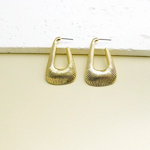 Vintage gold U-shaped geometric earrings with vertical textured stripes on stone surface