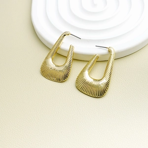 Macro detail of gold U-shaped earrings with fine vertical textures and metallic luster