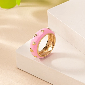 Détail d'une bague en émail rose avec des motifs de cœur dorés sur un support blanc