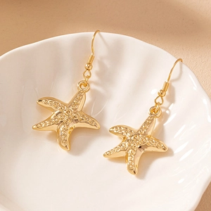 Detailed view of golden starfish earrings with textured surface on a white ceramic plate
