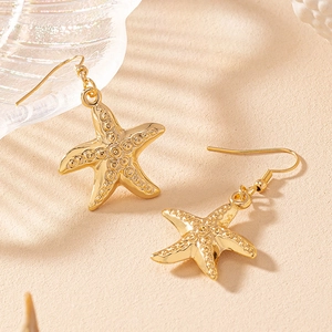 Elegant gold starfish drop earrings with textured finish on a sandy beach background