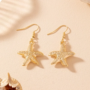 Golden starfish drop earrings with textured finish on sand background with shells