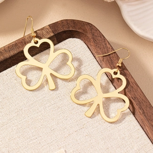 Minimalist gold clover drop earrings with hollow heart-shaped leaves on textured display