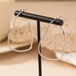 Orecchini a cuore argentati con texture glitterata esposti su supporto per gioielli