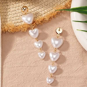 Elegant gold drop earrings with tiered white heart pearls on textured fabric background
