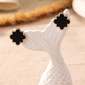 Chic black enamel flower stud earrings with gold plating on a white ceramic display