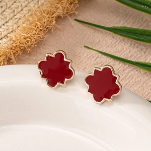 Detailed view of red floral enamel earrings with gold borders on white ceramic tray