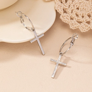 Boucles d'oreilles créoles croix argentées minimalistes sur textile beige et céramique