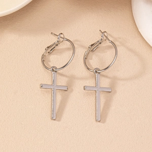 Détail des boucles d'oreilles créoles avec croix argentée sur un fond beige épuré