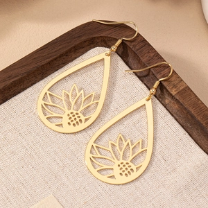 Boucles d'oreilles goutte dorées avec motif floral évidé sur fond texturé beige