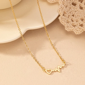 Collier élégant en or avec pendentif cœur et battement de cœur sur une surface beige clair