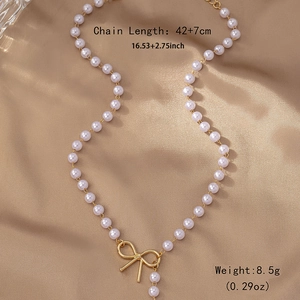 Elegant pearl necklace with gold bow pendant on champagne silk fabric, 42+7cm length