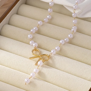 Elegant pearl necklace with golden bow pendant and tassel on a beige velvet background
