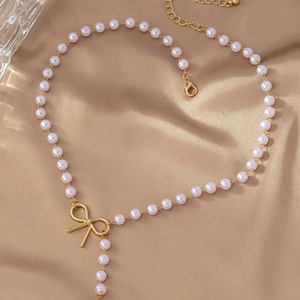 Close-up of pearl necklace with golden bow pendant on champagne silk background