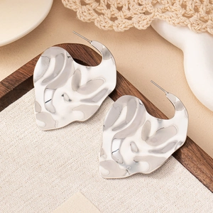 Boucles d'oreilles cœur irrégulières en métal liquide argenté sur un fond en bois rustique