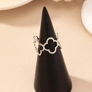 Fashionable hollow clover open ring in silver metal finish displayed on a dark stand