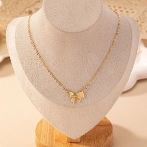 Élégant collier papillon doré présenté sur un support à bijoux en velours crème