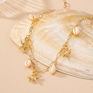 Golden starfish and white shell necklace displayed on a natural pearly seashell background
