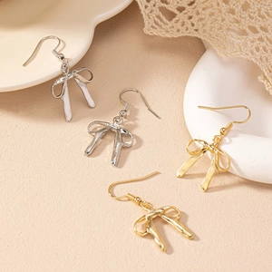 Détails de boucles d'oreilles nœuds dorées et argentées sur fond minimaliste doux